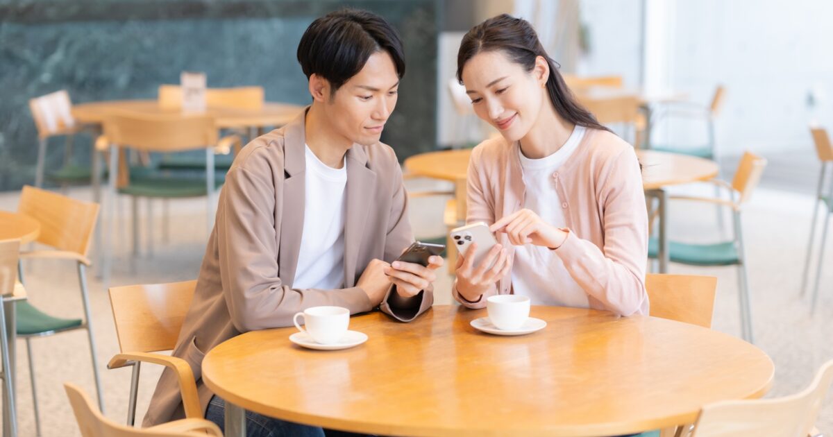 カフェでスマートフォンを見ながら話すカップル