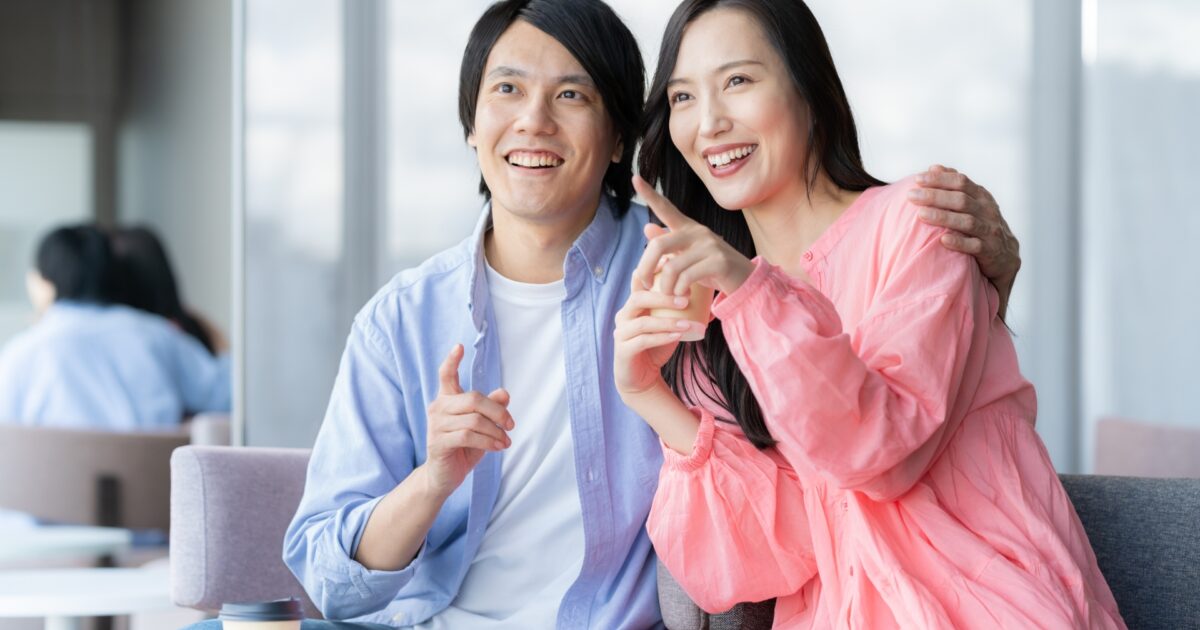 窓辺で寄り添いながら笑顔で指をさすカップル