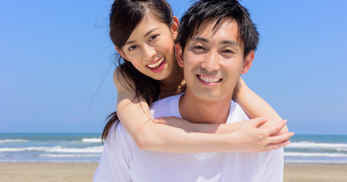 海辺でおんぶしながら笑顔を見せるカップル
