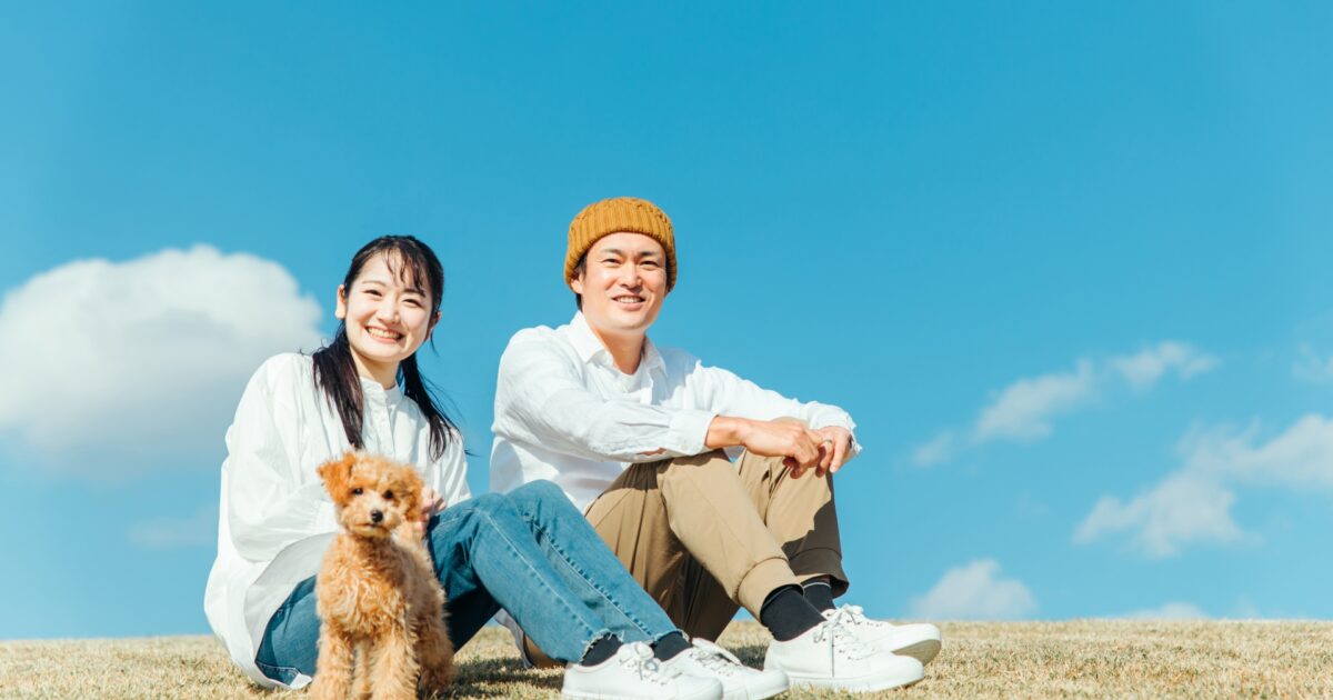 青空の下で愛犬と一緒に過ごすカップルの笑顔