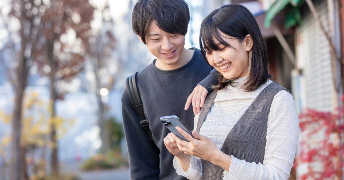 スマホを見ながら笑い合う秋服の若いカップル