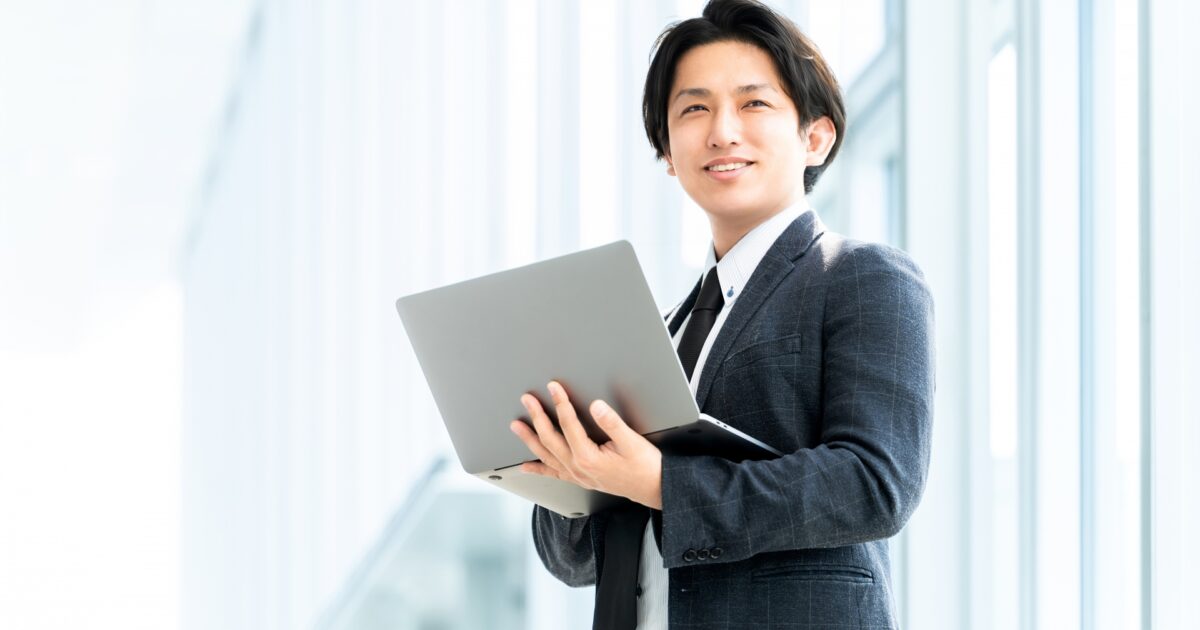 ノートパソコンを持ち自信を持って立つビジネスマン