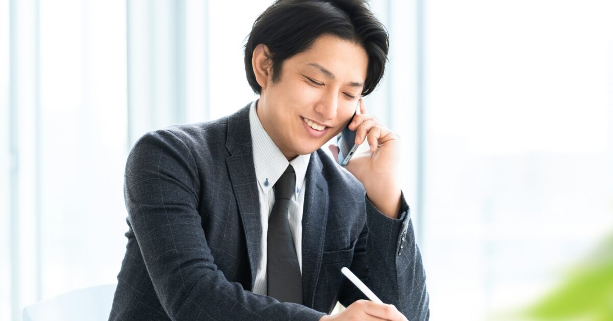 電話をしながらタブレットに書き込むビジネスマン