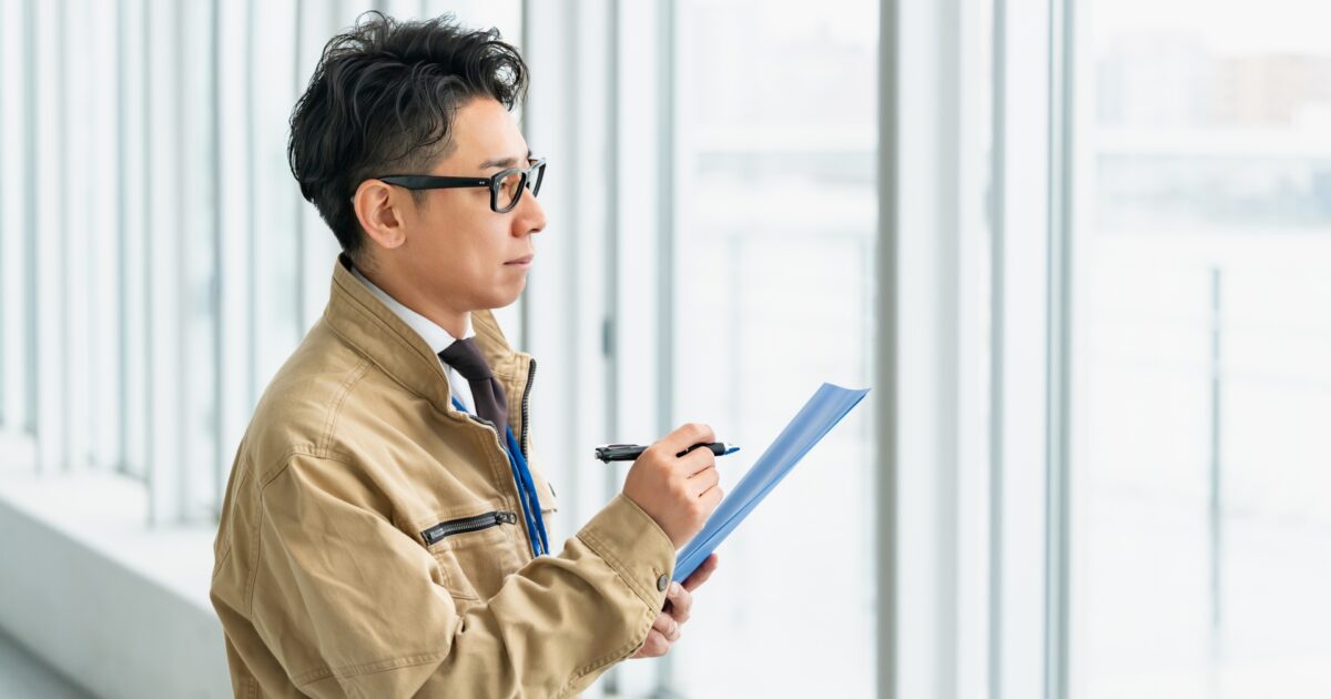 作業着姿で書類を確認する眼鏡の男性
