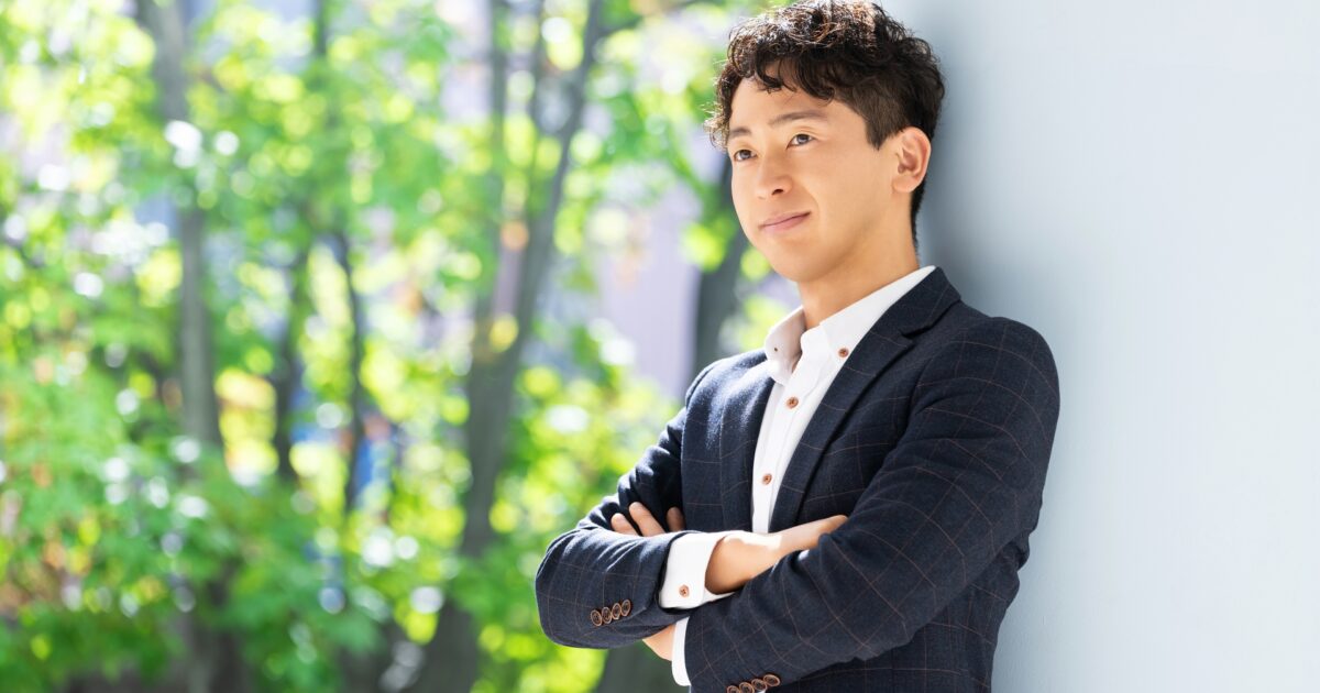 屋外で腕を組んで微笑むスーツ姿の若い男性