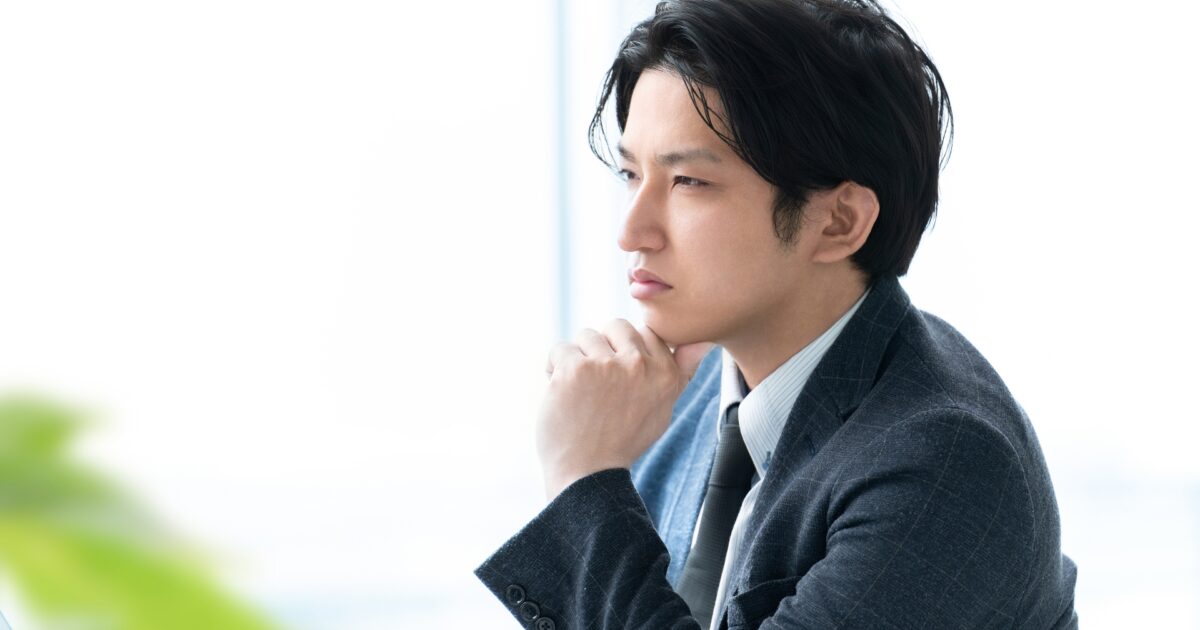 手を顎に当てて真剣に考えるスーツ姿の男性
